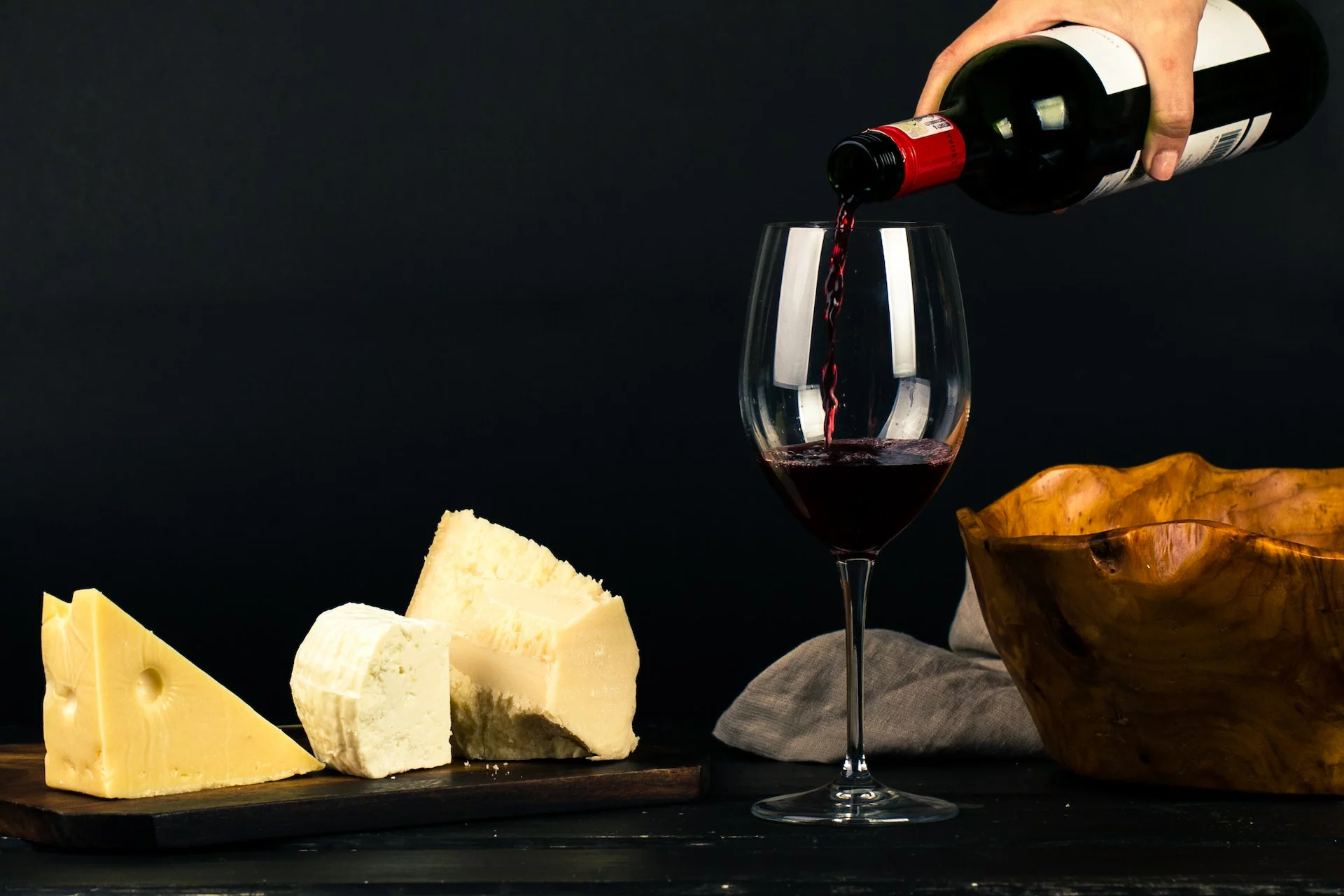 a person pouring wine into glass beside gruyère cheese